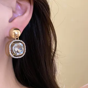 Close-up of elegant gold earrings with a clear crystal drop and pavé stones on a model.