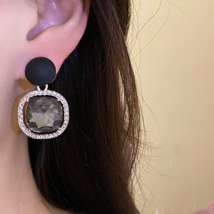 Close-up of matte black stud earring with rhinestone halo and gray crystal drop