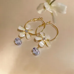 Detail shot of elegant gold hoop earrings featuring white resin flower and purple zircon drop