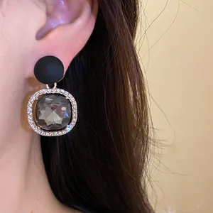 Close-up of elegant silver needle earring with grey faceted stone and crystal halo.