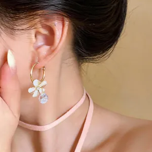 Close-up of elegant gold hoop earrings with white resin flower and sparkling zircon charm.