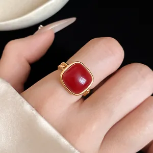 Gros plan d'une bague chaîne dorée ornée d'une pierre d'agate rouge en taille coussin.
