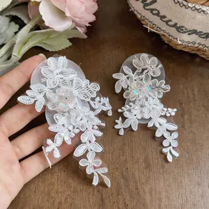 Close-up of white lace flower earrings with shimmering sequins and tassel details