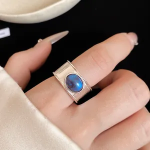 Gros plan d'une bague réglable argentée avec une pierre bleue ovale sur un doigt.