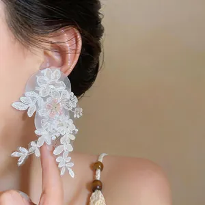 Close-up view of elegant white lace flower tassel earrings worn by a model in soft light