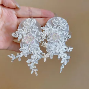 Detailed view of white lace floral earrings with sparkling sequin accents.