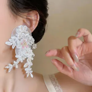 Detailed close-up view of delicate white lace flower earrings with shimmering pink sequins.