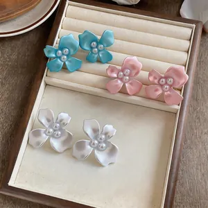 Detail view of flower-shaped stud earrings with pearl centers in blue, pink, and white