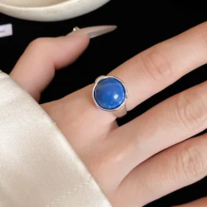 Gros plan d'une bague ouverte en argent ornée d'une pierre ronde bleue sur la main du modèle
