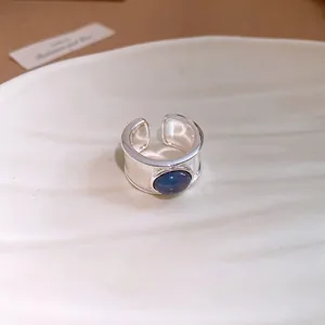 Gros plan détaillé d'une bague ouverte argentée avec pierre ronde bleu foncé sur coquillage