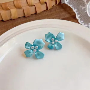 Macro detail of sweet blue flower stud earrings with pearl centers on white ceramic plate.