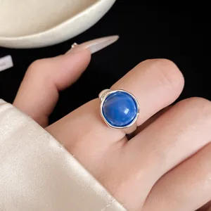 Gros plan d'une élégante bague réglable en argent avec une pierre bleue ronde au doigt
