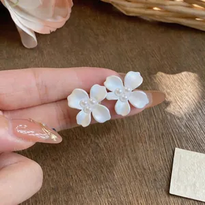 Detailed view of white flower stud earrings with pearl centers and silver needles