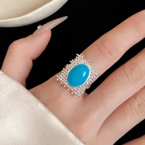 Détail d'une bague à pierre ovale bleue avec cadre en treillis argenté au doigt fin