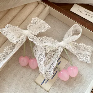 Close-up of white lace bow hair clips with pink cherry charms on a cream jewelry tray
