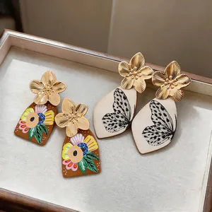 Dettaglio ravvicinato di eleganti orecchini a sospensione con fiori e farfalle dorate.