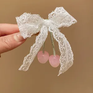 Close-up of a white lace bow hair clip with sweet pink cherry pendants.