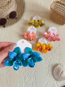 Boucles d'oreilles orchidées en résine bleue tenues à la main avec décor tropical.