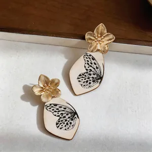 Dettaglio di orecchini a fiore dorato con pendente a motivo ala di farfalla nera