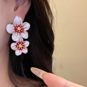 Elegant double layered white and red enamel flower earrings shown on a model's ear
