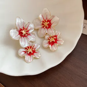 Close-up of elegant enamel flower earrings with red accents and golden stamens