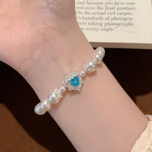 Close-up of elegant pearl bracelet with a sparkling blue heart crystal charm on wrist