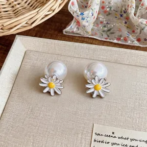 Elegant Korean style daisy flower and white pearl stud earrings on a textured background