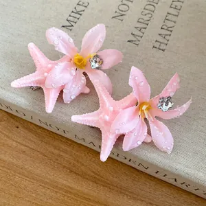 Detail view of pink starfish and flower hair clips with water droplet texture on a vintage book.