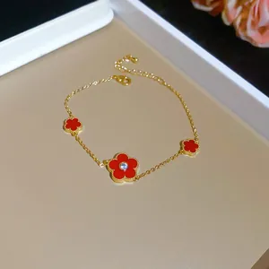 Close-up detail of an elegant gold-plated bracelet with red zircon flower charms.