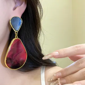 Close-up of vintage resin drop earrings with red marble pattern and gold frame worn by model