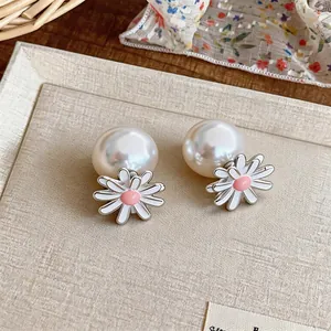 Detailed close-up of sweet enamel daisy and pearl stud earrings on a beige tray