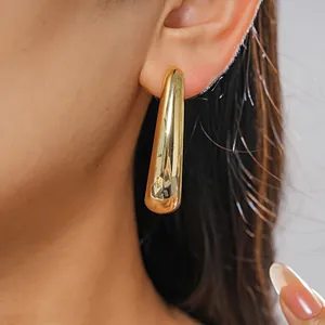 Close-up of polished gold drop earrings worn on ear showing sleek metallic texture