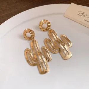 Detailansicht von goldenen Metallohrringen in Kaktusform auf einem weißen Porzellanteller