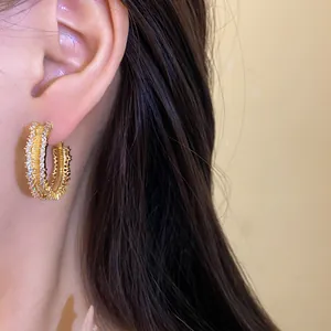 Detail showing the sparkling zircon and gold texture of the hoop earrings on a model's ear