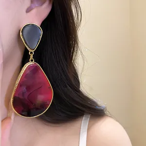 Close-up detail of a large resin water drop earring with marbled burgundy texture on a model's ear.