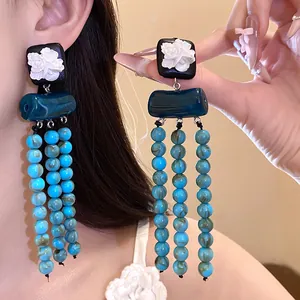 Detailansicht der ethnischen Vintage-Quastenohrringe mit weißen Harzblumen und blauen Perlen.