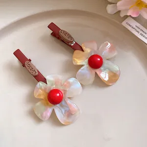 Dettaglio di fermagli per capelli a fiore in acetato iridescente con perle rosse.