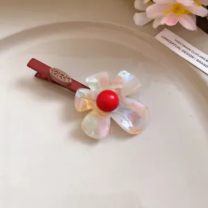 Dettaglio fermaglio per capelli a fiore in acetato iridescente con perla rossa.
