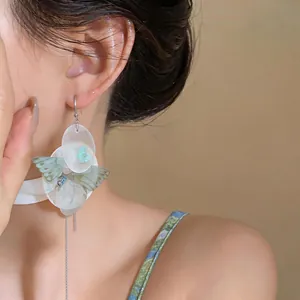 Close-up detail of elegant chiffon butterfly and shell flower tassel earrings on model