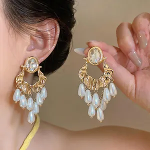 Close-up detail of oversized gold-tone earrings with oval rhinestones and pearl fringe