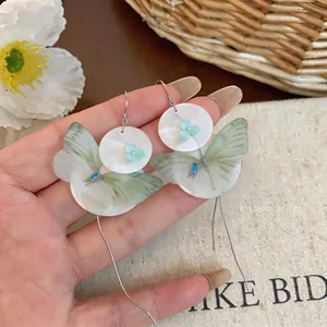 Detailed macro view of chiffon butterfly and shell disk earrings with long tassels