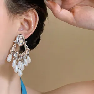 Detailed close-up view of vintage oval rhinestone and pearl tassel earrings worn by a model