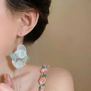 Detail view of elegant chiffon butterfly and shell flower tassel earrings on a model
