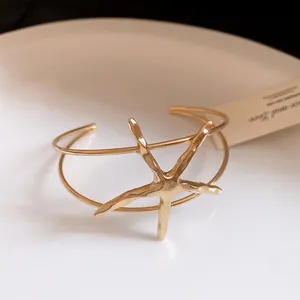 Macro view of a gold-toned starfish open cuff bracelet with textured metallic finish