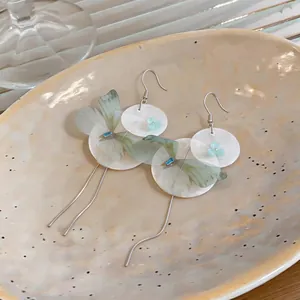 Macro view of delicate chiffon butterfly wings and shell flower detail on these earrings.