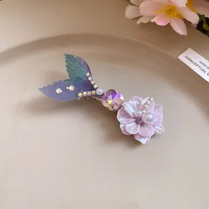 Primo piano di un fermaglio per capelli in acetato con coda di sirena e fiori colorati.
