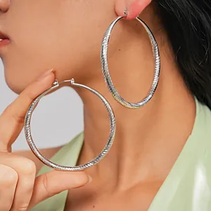 Close-up of large silver faceted metal hoop earrings on model showing textured detail