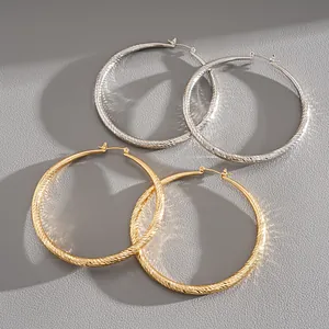 Detail view of textured gold and silver hoop earrings on grey leather background.