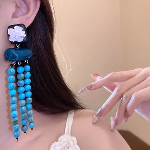 Nahaufnahme von ethnischen Blumenohrringen mit blauen Marmorperlen an einem Modell.