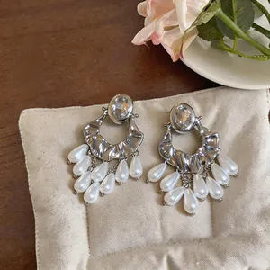 Detailed view of silver-toned drop earrings featuring oval crystals and pearl tassels